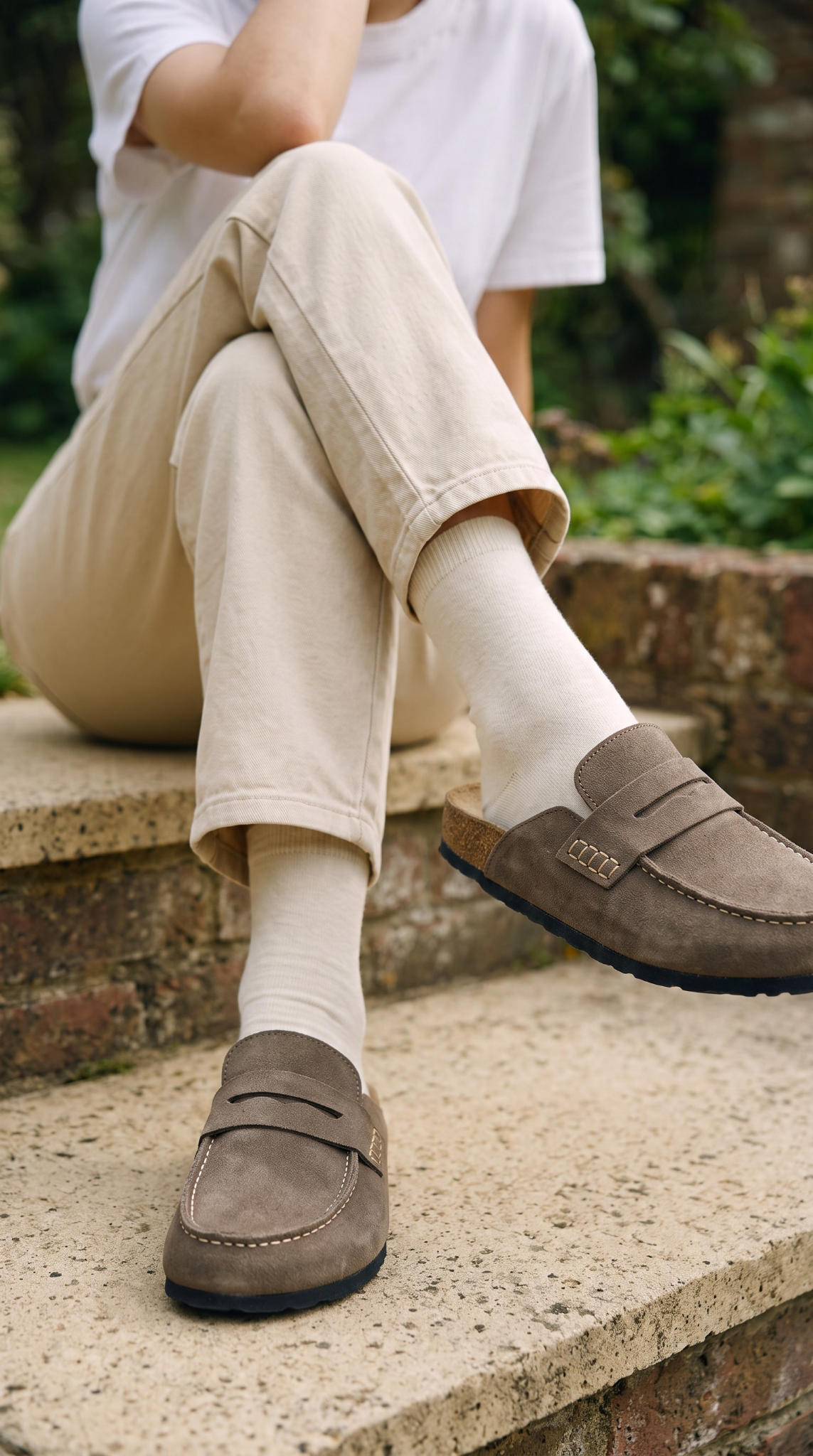 Mules Avern Stone Taupe portées avec des chaussettes écrues sur un escalier en pierre
